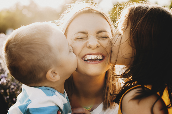 Image of young children kissing their smiling mother on the cheeks